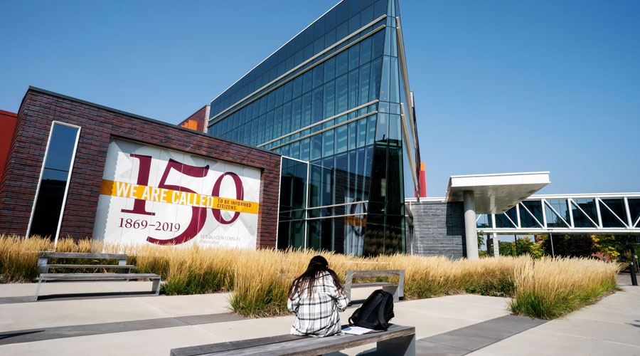 A student studying on a bench outside of Hagfors Center with a clear blue sky